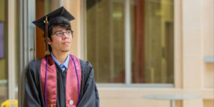 Dell Scholar stands in graduation cap outside his university