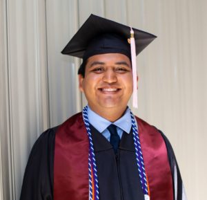 A Dell Scholars student stands in his cap and gown on college graduation day